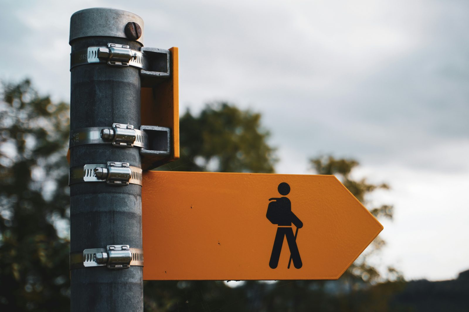 An orange trail directional sign with a hiker silhouette mounted on a metal post