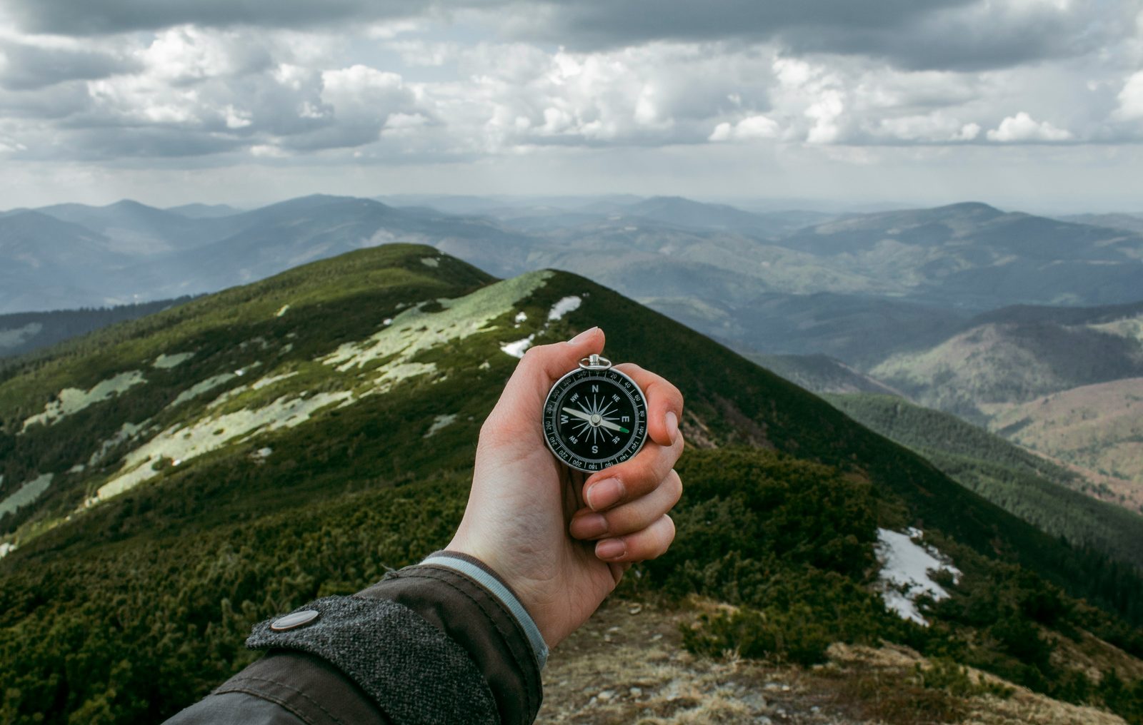 A hand holding a compass against a sweeping mountain landscape and cloudy sky